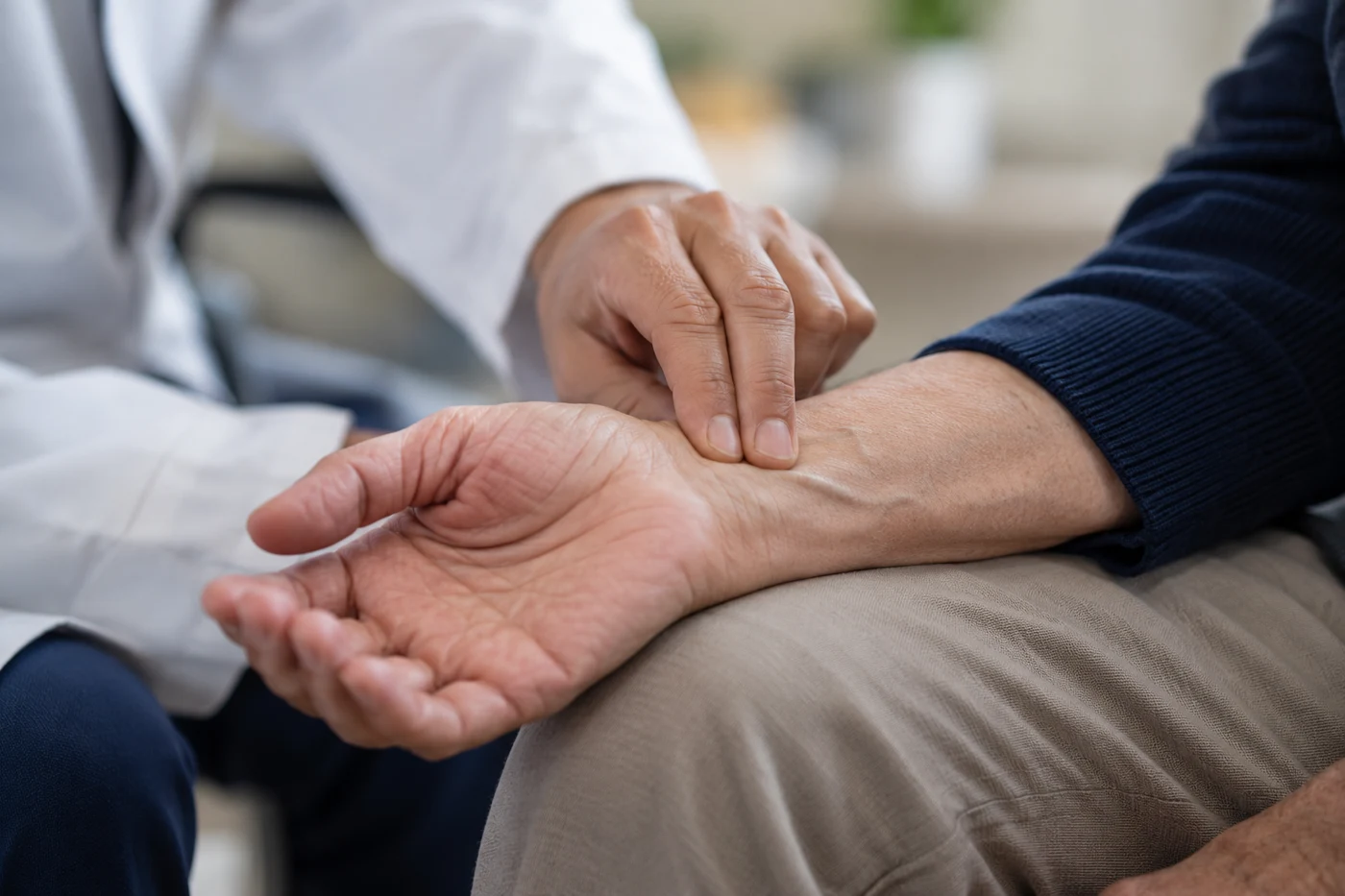 Close-up clinician fingers checking an older adult radial pulse at wrist, natural skin textures, navy cuff. Illustrative editorial photograph.